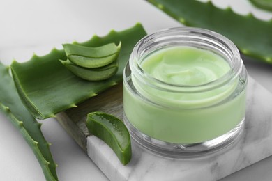 Jar with cream and cut aloe leaves on white table, closeup