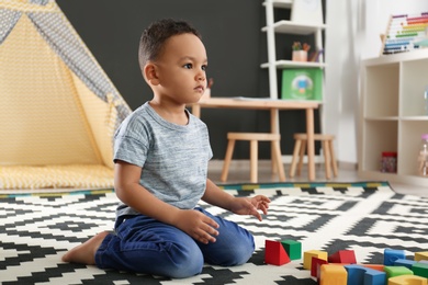 Photo of Cute little African-American child playing with building blocks on floor in kindergarten. Indoor activity