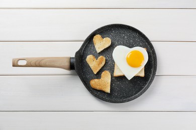 Romantic breakfast with heart shaped fried egg and toasts in pan on white wooden table, top view