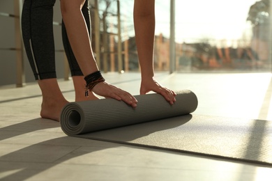 Photo of Young woman rolling yoga mat in sunlit room, closeup