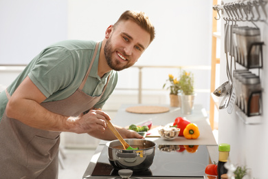 Photo of Young man cooking delicious soup in kitchen