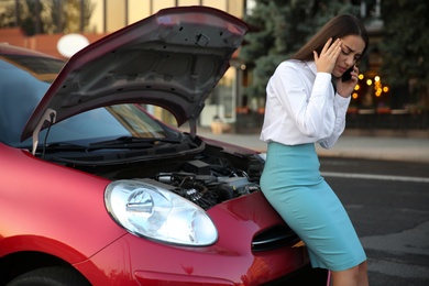 Photo of Stressed woman talking on phone near broken car outdoors