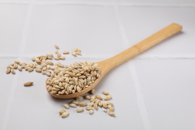 Photo of Wooden spoon with dry pearl barley on white tiled table, closeup