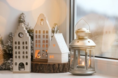 Photo of Beautiful house shaped candle holders and Christmas decor on windowsill indoors. Bokeh effect