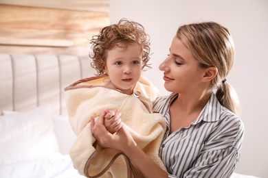 Photo of Mother holding cute little baby wrapped with hooded towel after bath indoors