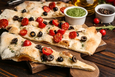 Focaccia bread with olives and tomatoes on wooden table, closeup