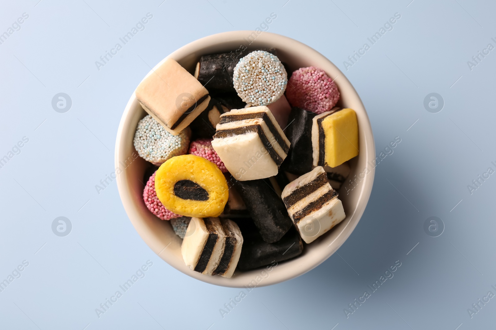 Photo of Bowl of tasty liquorice candies on light blue background, top view