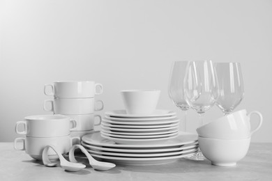 Set of clean dishware and glasses on grey table against light background