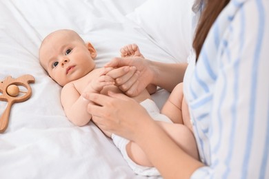 Woman applying body cream onto baby`s skin on bed, closeup