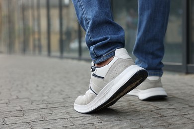 Photo of Man in jeans and sneakers walking on city street, closeup. Space for text