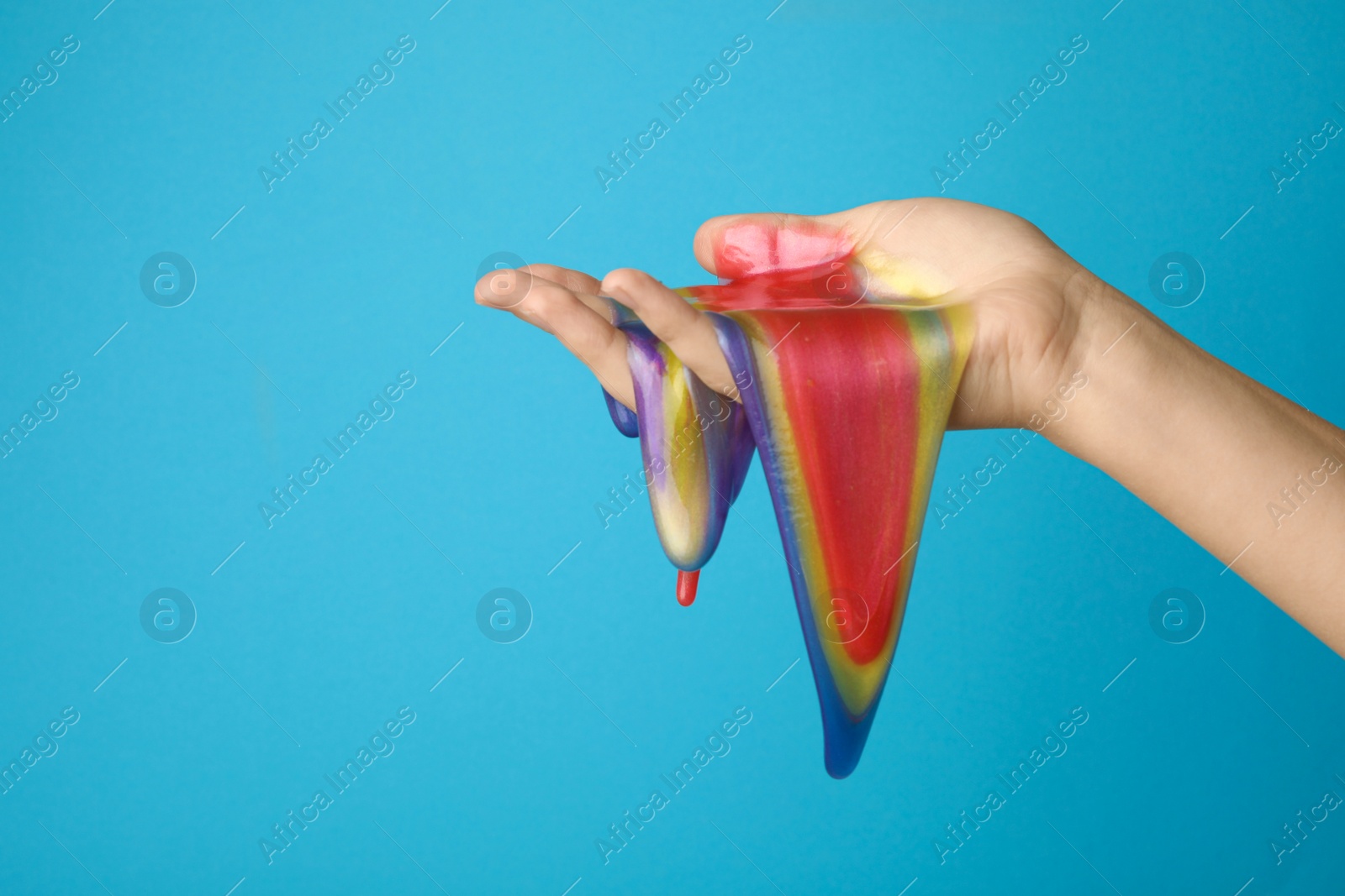 Photo of Woman playing with colorful slime on light blue background, closeup. Antistress toy