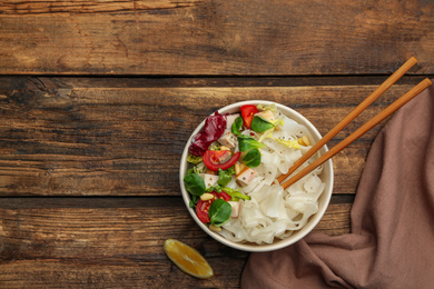 Photo of Tasty cooked rice noodles with chicken and vegetables on wooden table, flat lay