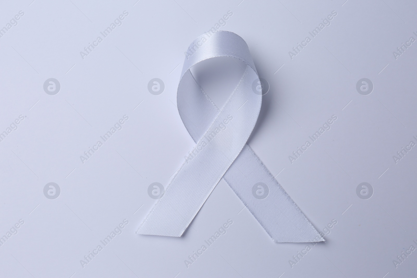 Photo of White awareness ribbon on white background, top view