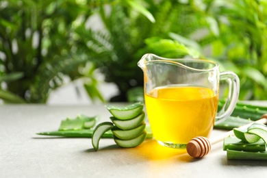 Photo of Fresh aloe vera leaves and jug of honey on table against blurred background with space for text