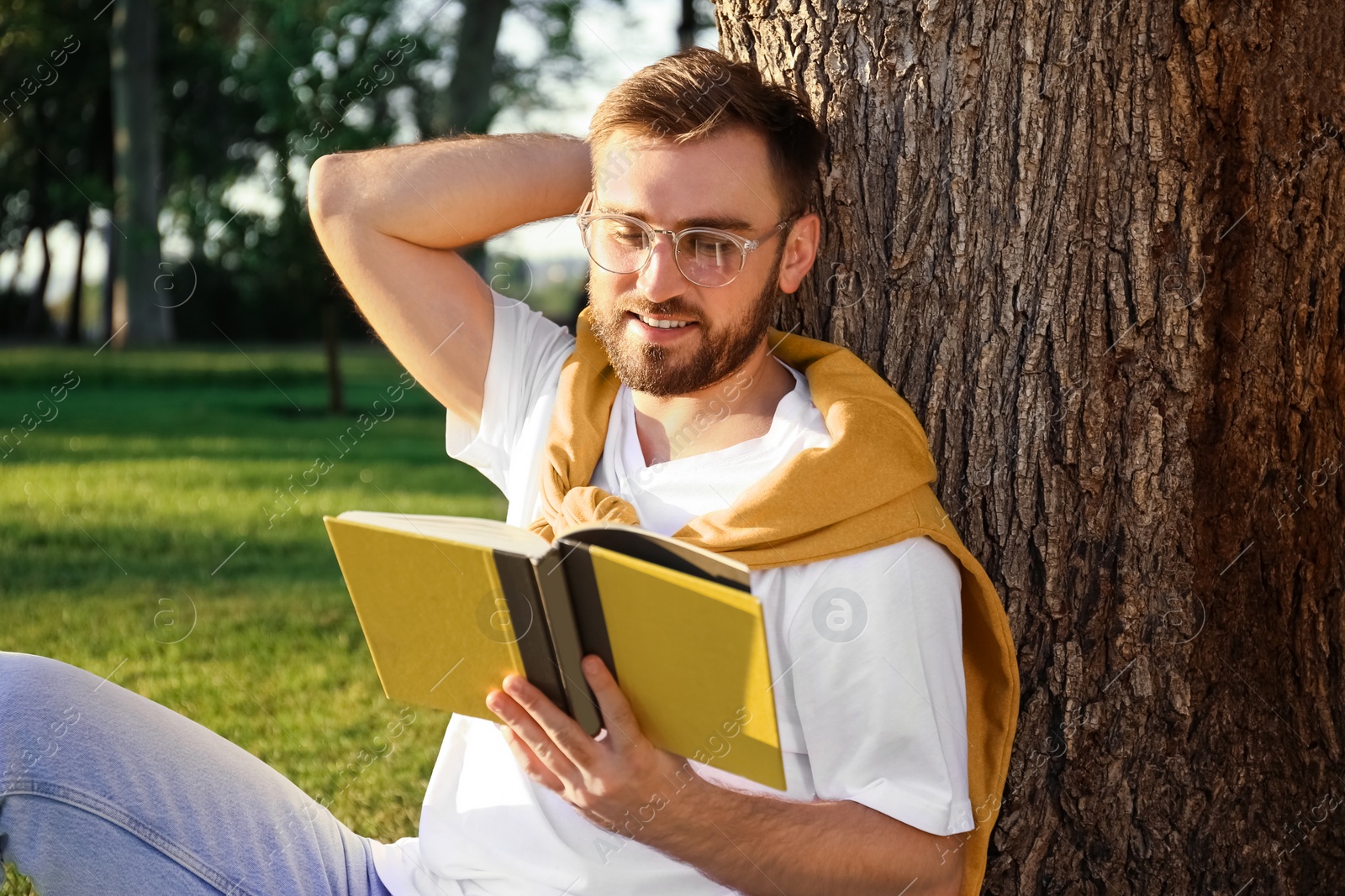 Photo of Young man reading book near tree in park