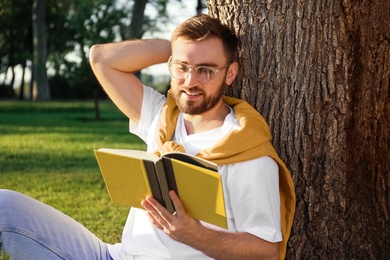 Young man reading book near tree in park