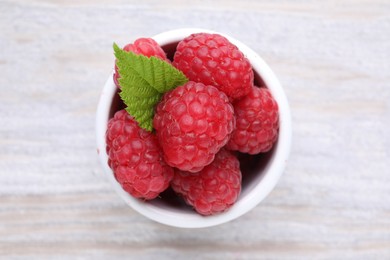 Photo of Tasty ripe raspberries and green leaf on white wooden table, top view