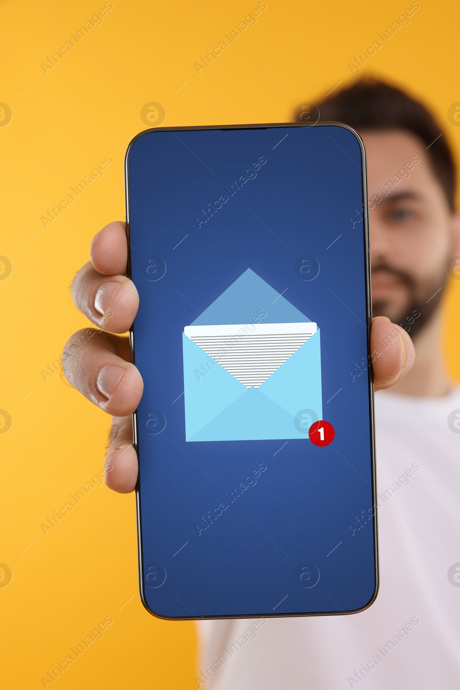 Image of Man showing mobile phone with new message notification on screen against yellow background, selective focus