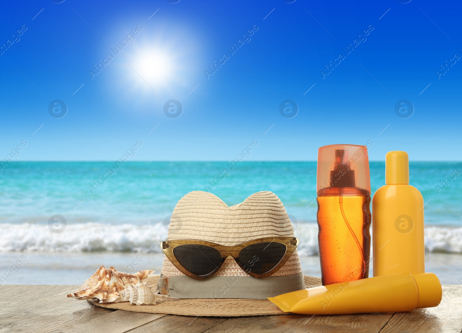 Image of Skin sun protection products and beach accessories on wooden table against seascape. Space for design