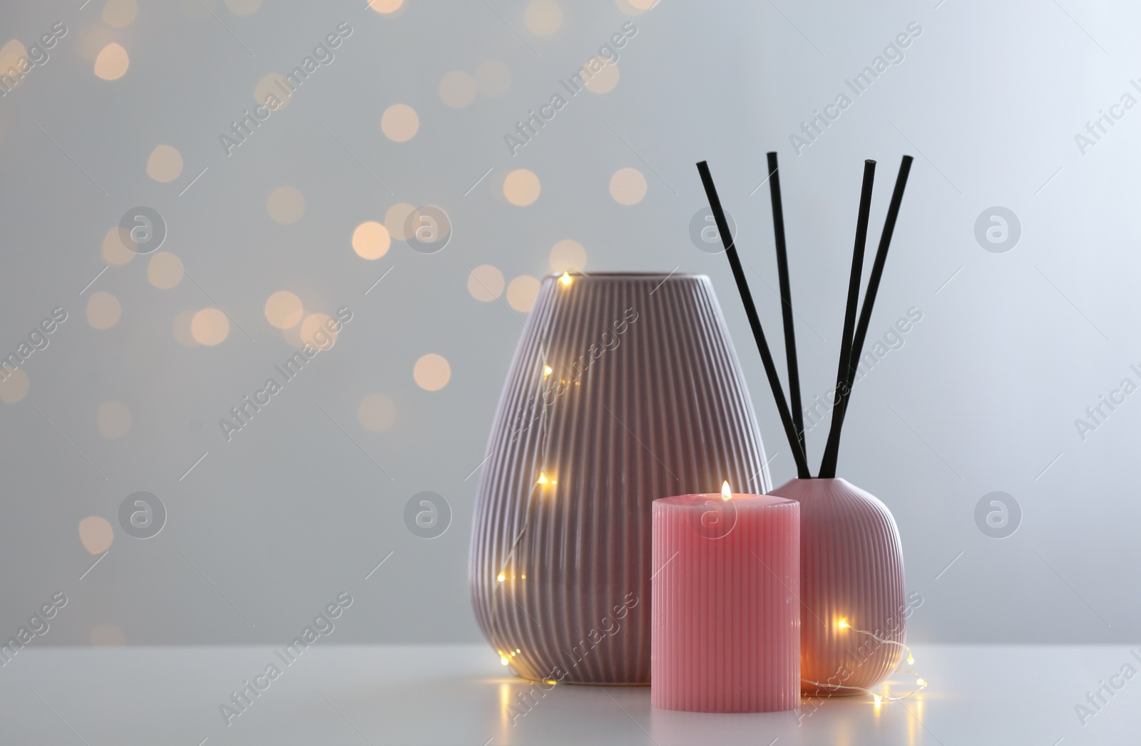 Photo of Vase, burning candle and reed diffuser on table against blurred background with bokeh effect. Space for text