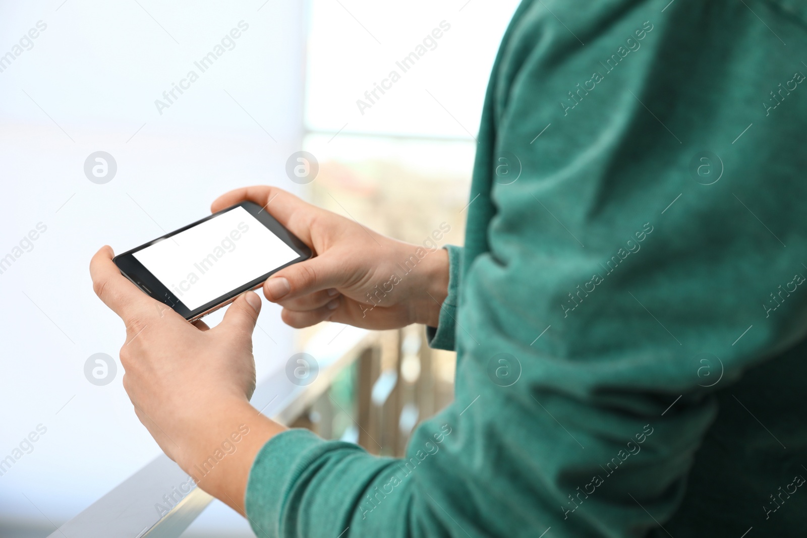 Photo of Man holding smartphone with blank screen indoors, closeup of hands. Space for text