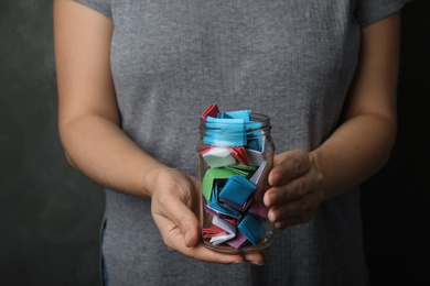 Photo of Woman holding glass jar with colorful paper pieces, closeup on hands
