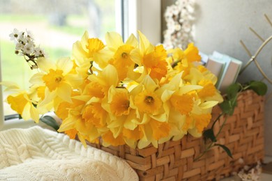 Photo of Beautiful yellow daffodils in wicker basket near window, closeup
