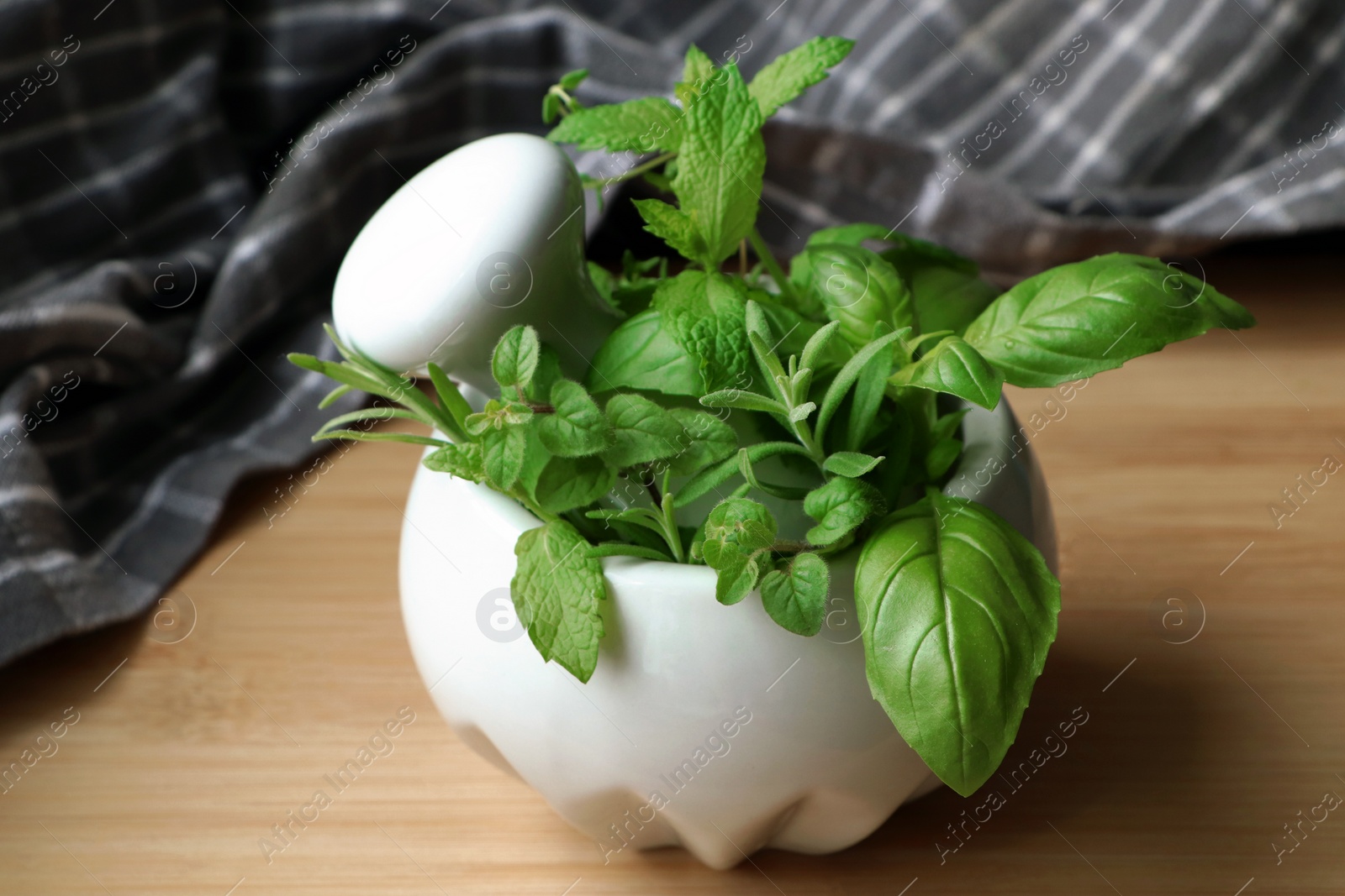 Photo of Mortar with different fresh herbs on wooden table, closeup