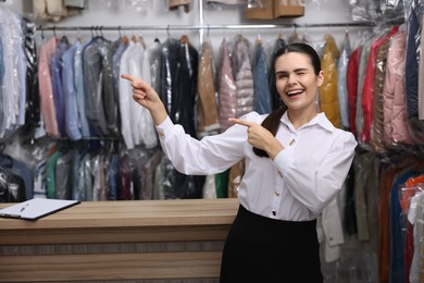 Photo of Dry-cleaning service. Happy worker pointing something near counter indoors, space for text