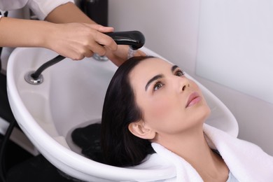 Photo of Professional hairdresser washing woman's hair in beauty salon, closeup