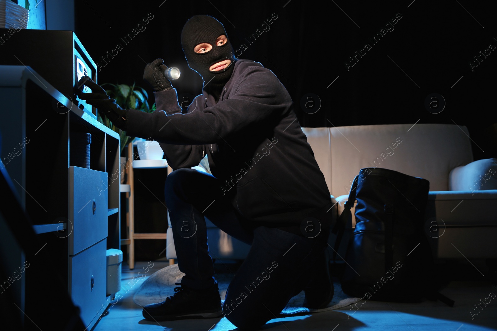 Photo of Thief with flashlight near steel safe indoors at night