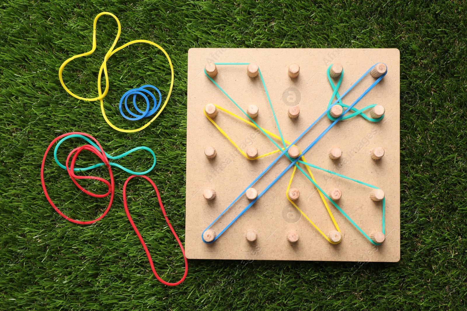 Photo of Wooden geoboard with dragonfly made of rubber bands on artificial grass, flat lay. Educational toy for motor skills development