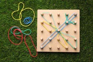 Photo of Wooden geoboard with dragonfly made of rubber bands on artificial grass, flat lay. Educational toy for motor skills development
