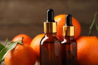 Photo of Bottles of tangerine essential oil and fresh fruits on table, closeup
