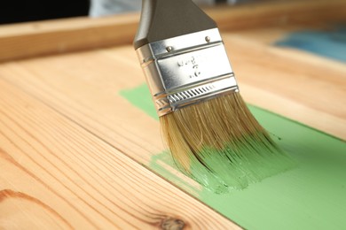 Photo of Applying green paint onto wooden surface, closeup. Space for text