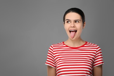 Photo of Happy young woman showing her tongue on grey background. Space for text