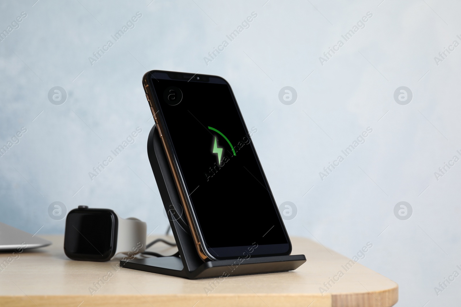Photo of Mobile phone charging with wireless pad and smartwatch on wooden table