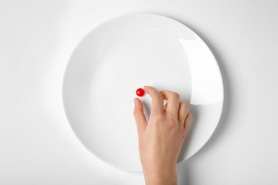 Photo of Woman taking weight loss pill from plate on white background, top view