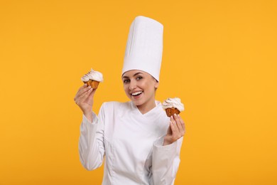 Photo of Happy professional confectioner in uniform holding delicious cupcakes on yellow background