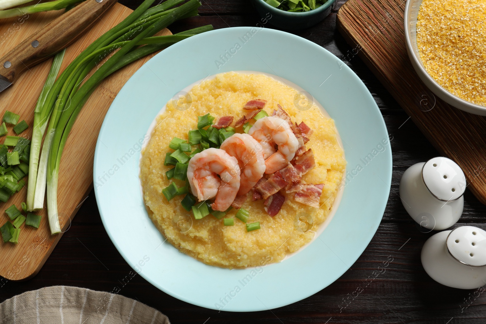 Photo of Plate with fresh tasty shrimps, bacon, grits and green onion on dark wooden table, flat lay