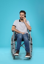 Young man in wheelchair talking on phone against color background