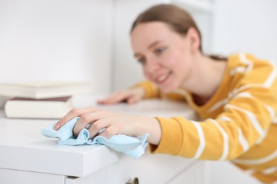 Woman cleaning chest of drawers with rag at home, selective focus