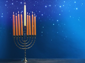 Image of Hanukkah celebration. Menorah with burning candles on wooden table against blue background, space for text