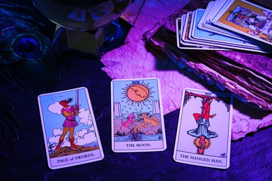 Photo of Page of Swords, Hanged Man and Moon tarot cards on dark table, color toned