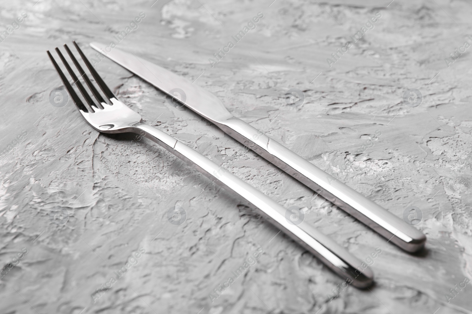 Photo of Stylish cutlery. Silver knife and fork on grey textured table, closeup