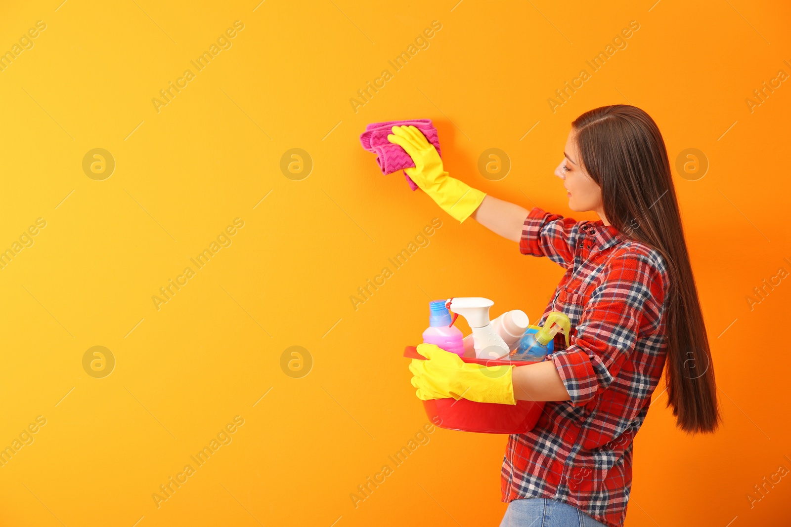 Photo of Young woman cleaning color wall with rag