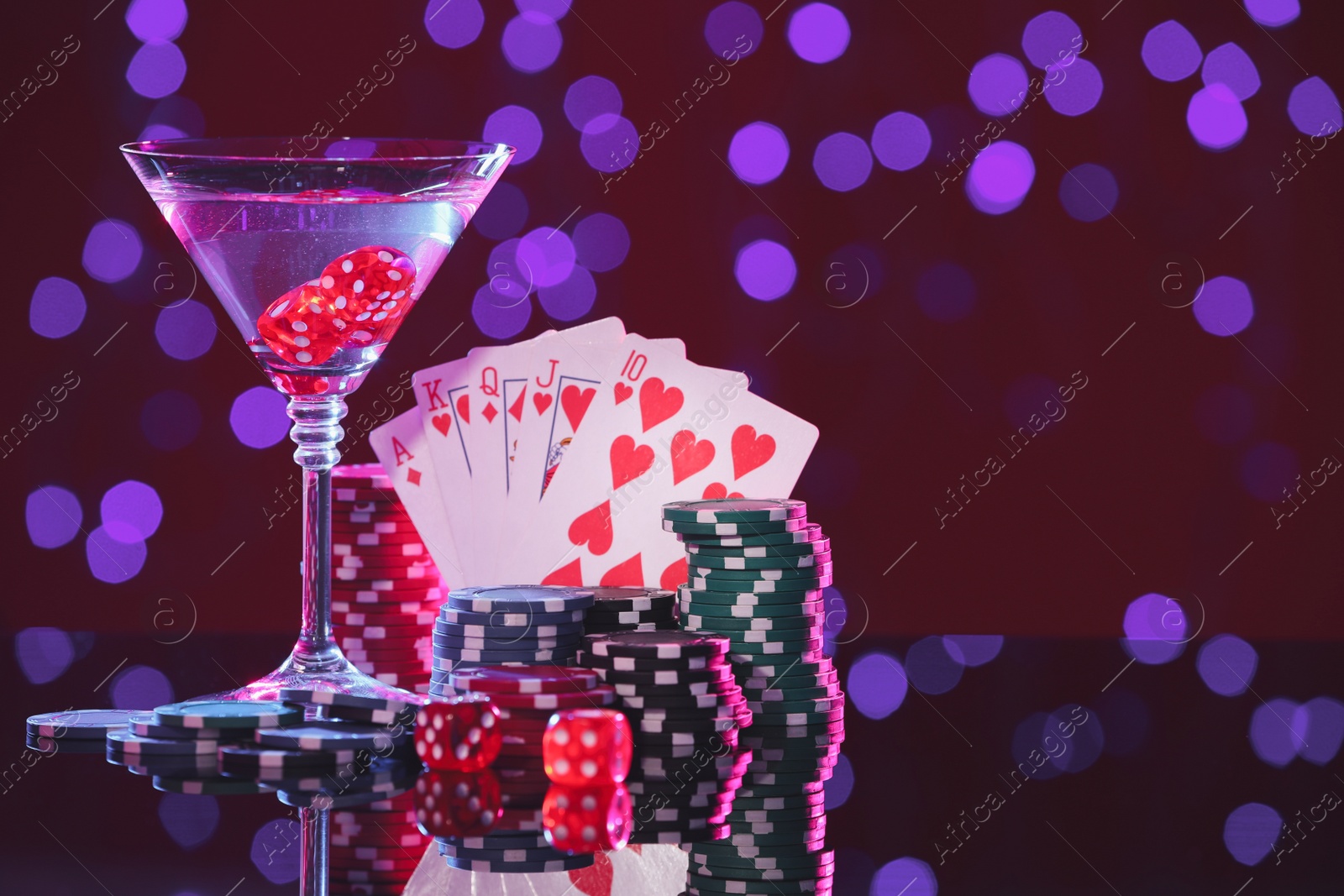 Photo of Alcohol drinks, dice, playing cards and casino chips on table against blurred lights, space for text. Straight poker combination