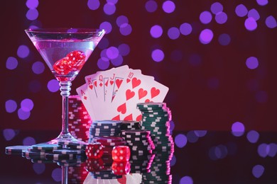 Photo of Alcohol drinks, dice, playing cards and casino chips on table against blurred lights, space for text. Straight poker combination