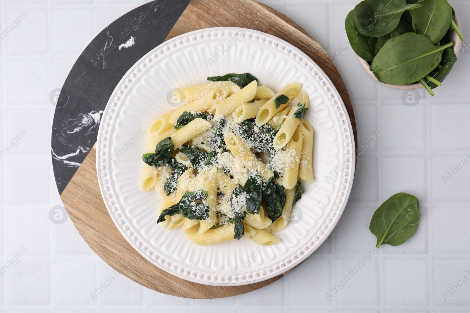 Photo of Tasty pasta with spinach and cheese on white tiled table, flat lay