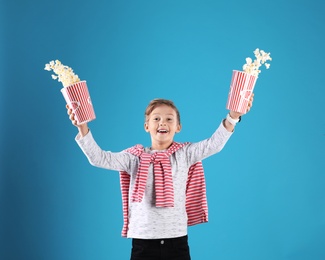 Cute boy scattering popcorn from buckets on color background
